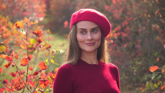 Young beautiful sensual woman in a red sweater and beret posing in the autumn forest, against a background of red foliage. Fashionable video portrait