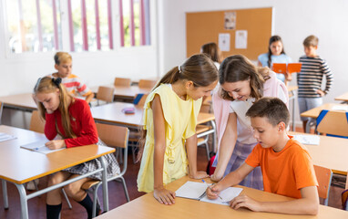 Young girls and boys performing tasks in school together, writing in copybook.