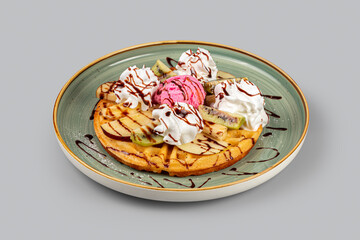 Dessert on a plate. Waffles with pieces of fruit and ice cream on a light gray background