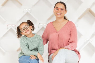 Family, eye care and glasses on mother and child in optics store for shopping, optometry and health care while advertising lens or frame choice. Portrait of woman and girl happy with vision insurance