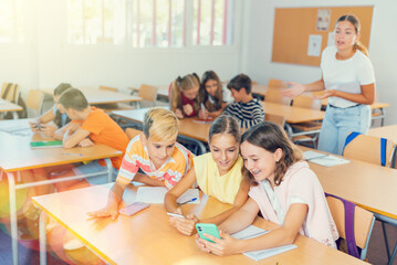 Group of kids using smartphones during lesson in school. Girls and boys using gadgets while...