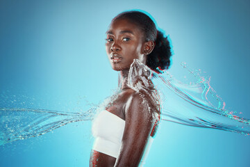 Skincare, water and black woman with a splash for hydration, cleaning and beauty against a blue studio background. Spa, wellness and African model with peace, calm and relax from liquid bodycare