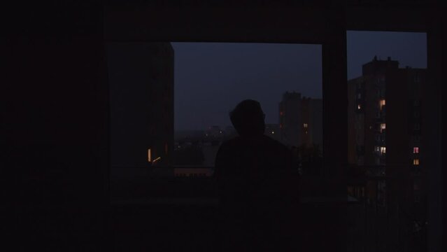 Man Looking Out A Window During Storm In City Back View