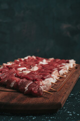 Raw meat on black background. Small pieces of raw meat on wooden skewers 
