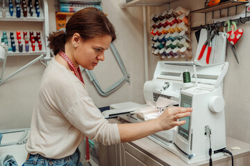 A woman tailor makes embroidery on an embroidery machine in a home workshop.Mending clothes concept,small business. - obrazy, fototapety, plakaty