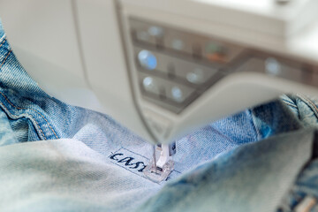 An embroidery machine embroider a pattern on jeans.Mending clothes concept,reusing old jeans.Selective focus,close-up. - obrazy, fototapety, plakaty