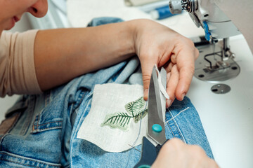 A woman mends jeans, sews a patch on a hole, hands close-up.Mending clothes concept,reusing old jeans. - obrazy, fototapety, plakaty
