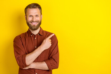 Portrait of optimistic toothy beaming man with masculine beard burgundy shirt indicating empty space isolated on yellow color background