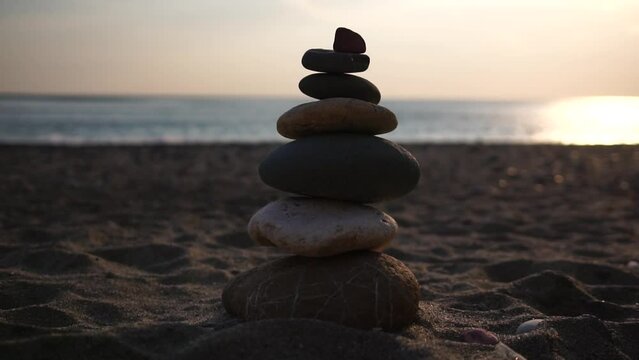 Balanced pebbles pyramid on the beach on sunny day and clear sky at sunset. Golden sea bokeh on background. Selective focus, zen stones on sea beach, meditation, spa, harmony, calm, balance concept.