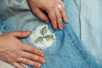 A woman mends jeans, sews a patch on a hole, hands close-up.Mending clothes concept,reusing old...