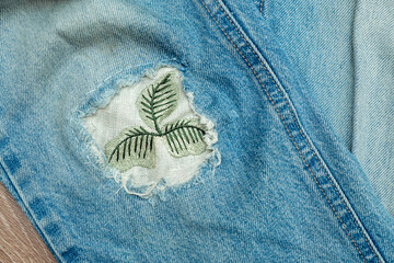 Old worn jeans with a patch sewn in place of a hole.Mending clothes concept.Reusing old jeans.Sustainable fashion, - obrazy, fototapety, plakaty
