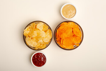 Paprika flavored potato chips and original chips with salt in small glass bowls, two kind of sauces from above on a light beige background. Snacks for group of people.