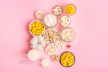 Organic food supplements in jars and small plates on pink background from above. Different vitamins and minerals to improve human`s health and immune system.