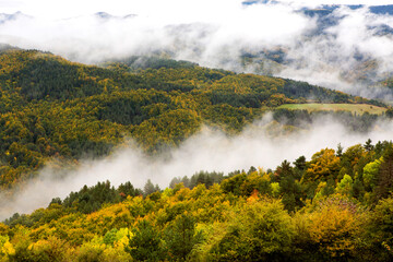 Autumn mountains and hills with colorful trees and low clouds and fog between them in Irati forest