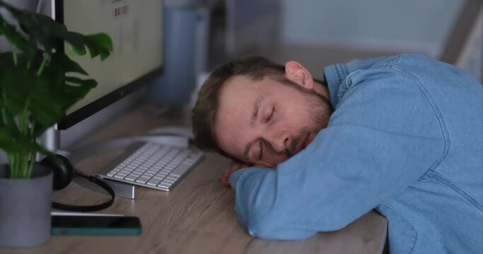 Software developer of web designer: caucasian bearded tired IT guy sleeping and awaking at working place in office. Man sleeping at desk, tired of stressful job burnout at work, lack energy. 4k video