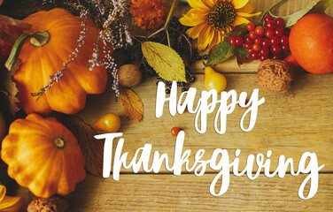 Happy Thanksgiving greeting card. Happy Thanksgiving text on stylish pumpkins, autumn flowers, berries and nuts composition on rustic wooden table. Handwritten lettering © sonyachny