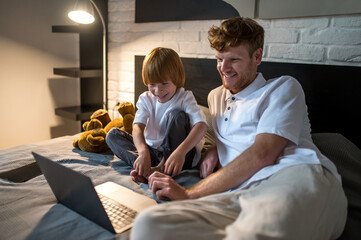 Dad and son lying in bed and watching something online before sleep