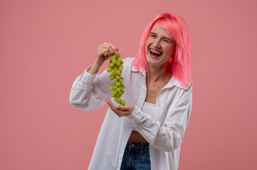 Laughing pink-haired girl holding a grapevine in her hands