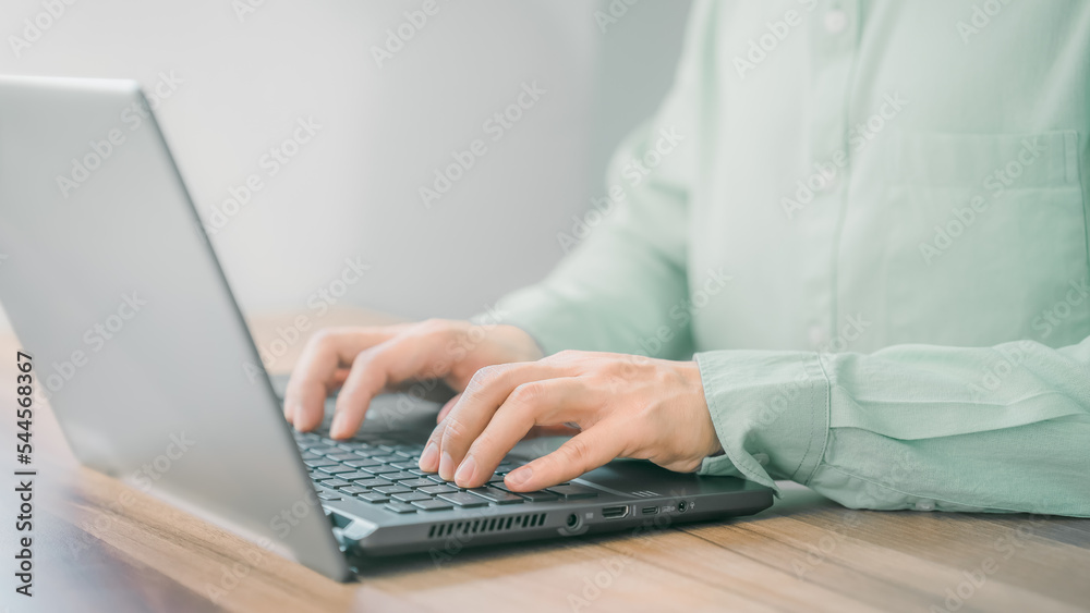 Poster Closeup image of a young man working and typing on laptop computer keyboard on wooden table in the room.
