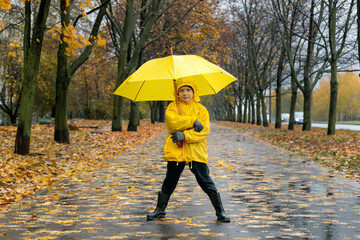 Little boy in yellow raincoat with an yellow umbrella in park . Child walking on rainy autumn street