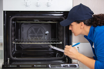 female technician with clipboard inspecting oven - Powered by Adobe