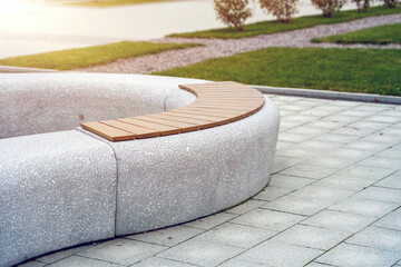 Curiously curved concrete bench with wooden slats for sitting in a city park in autumn