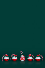 Christmas bells and Lucky cat figure in a row on green background with copy space. Christmas theme. Four red-white decorating jingle bells with swirl ribbons and red-white Lucky cat between them.