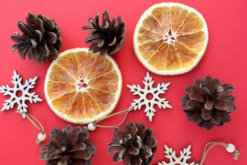 Cones, dry oranges and wooden snowflakes on a red background. Holidays.