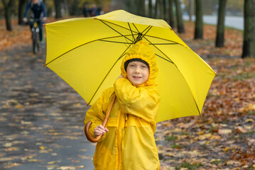 Portrait of smiling boy in yellow raincoat with large yellow umbrella in the autumn park. Happy...