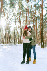 Young happy couple are standing and hugging on sunny day in snow-covered park. Portrait of men and women in a snowy winter park. Vertical frame