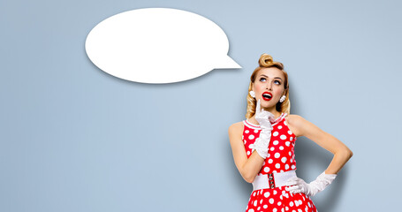Studio portrait image of thinking woman in red pin up dress. Blond pinup thougthfull girl over grey background. White empty blank speech sign bubble, having idea.