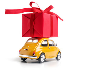 Yellow retro toy car delivering red gift box with ribbon on a white background.