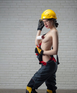 sexy girl with bare breasts in a construction helmet and clothes with a paint roller in her hands