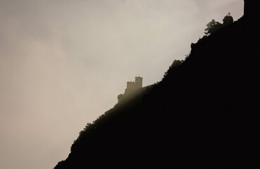 Castillo medieval visto en medio de la niebla, contrastando contra la colina oscura