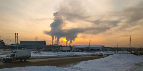 Traffic of cars on a suburban highway against the background of smoke from a thermal power plant and against the background of the evening sky at sunset
