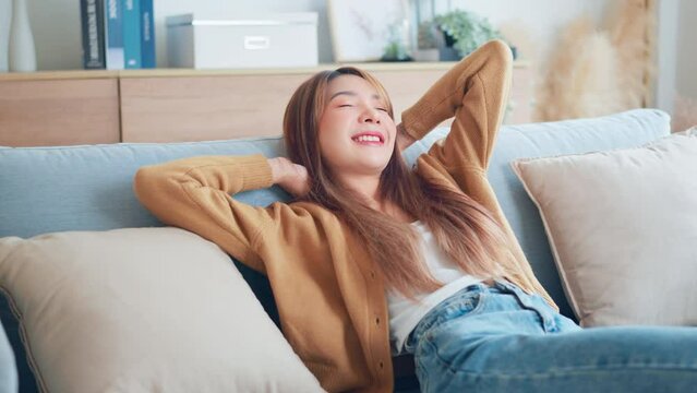 Relaxed young asian woman enjoying rest on comfortable sofa at home, calm attractive girl relaxing and breathing fresh air in home.