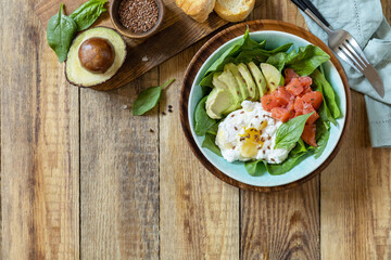 Delicious breakfast or lunch bowl with salted salmon fish, avocado, boiled egg and spinach on a rustic table. Ketogenic, keto or paleo diet. View from above. Copy space.