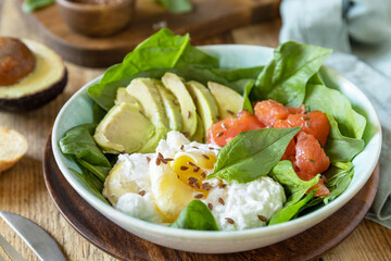 Delicious breakfast or lunch bowl with salted salmon fish, avocado, boiled egg and spinach on a rustic table. Ketogenic, keto or paleo diet.