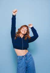 Happy young woman dancing and having fun while wearing a crop top and jeans in a studio