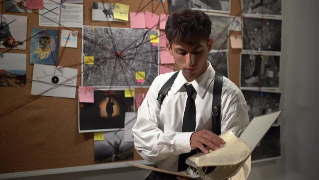 Concentrated detective in black suit reading dossier in dark office. Investigator working with criminal case documents.