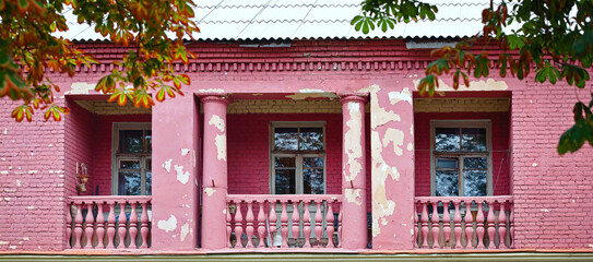 Fototapeta na wymiar Old balcony with column and balustrade. Old balcony on purple building facade with cracked stucco wall