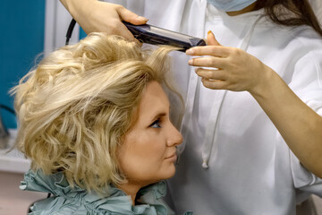 Fototapeta premium The hairdresser does the styling of the girl before the holiday party in the beauty salon. Creating a hairstyle.