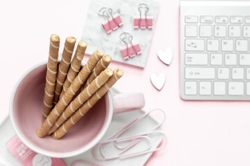 A feminine woman workspace, with a silver keyboard of a computer on a pastel pink background with copy space. Banner image with candle and other office space and desktop white stationery