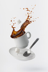 coffee poured from a floating cup with a teaspoon and sugar cubes isolated on white background