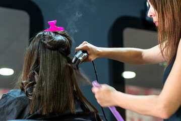 Fototapeta premium Hairdresser straightening long brown hair with hair irons.