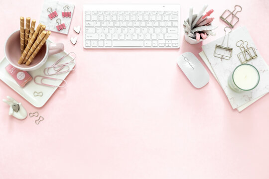 A feminine woman workspace, with a silver keyboard of a computer on a pastel pink background with copy space. Banner image with candle and other office space and desktop white stationery