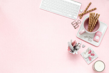 A feminine woman workspace, with a silver keyboard of a computer on a pastel pink background with...