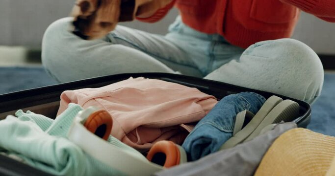 Hands, luggage and travel with a woman packing clothes for a trip, holiday or vacation on a floor at home. Journey, baggage and suitcase with a female traveler putting clothing in a bag for tourism