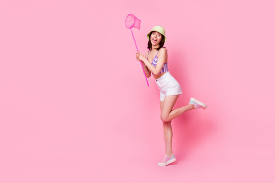 Full size photo of pretty young girl hold net catch insect enjoy nature banner dressed trendy singlet cap isolated on pink color background