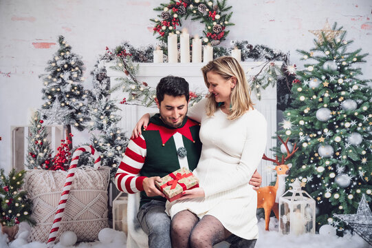 Couple in Christmas outfits jumper dress festive gifting wrapped present box decoration background white bright studio picture 